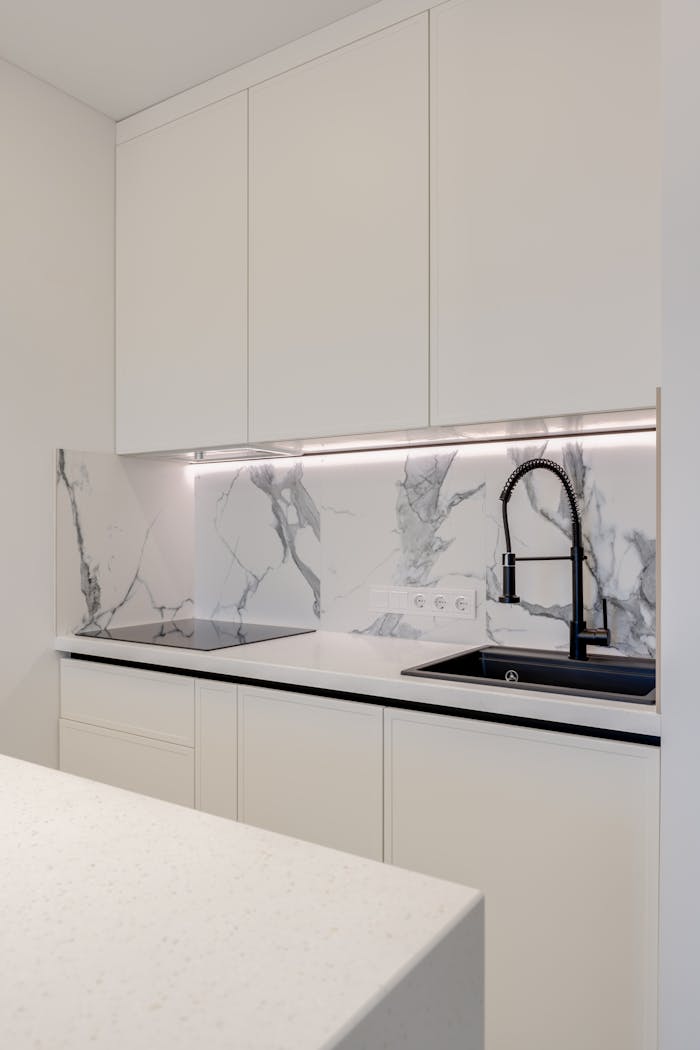 Elegant kitchen featuring white cabinets, marble backsplash, and a black sink.