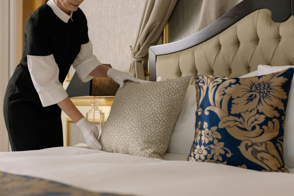 pexels-photo-6466496-6466496 A chambermaid arranges pillows in a luxurious hotel room, showcasing comfort and elegance.